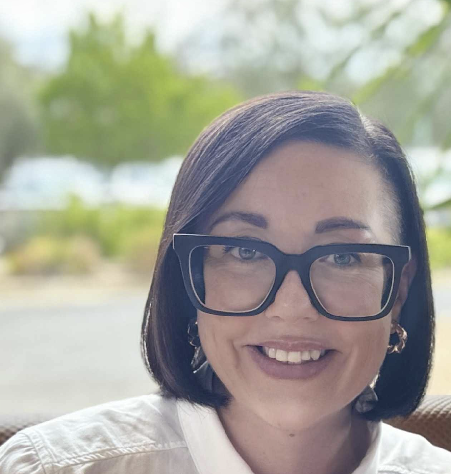 Smiling person with glasses outdoors.