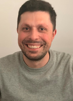 Smiling man in grey shirt, neutral background.