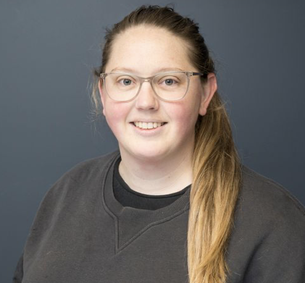 Person with glasses smiling, wearing a grey jumper.