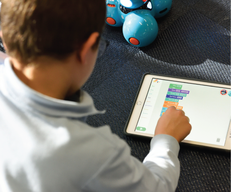 Child coding on tablet with robot nearby.