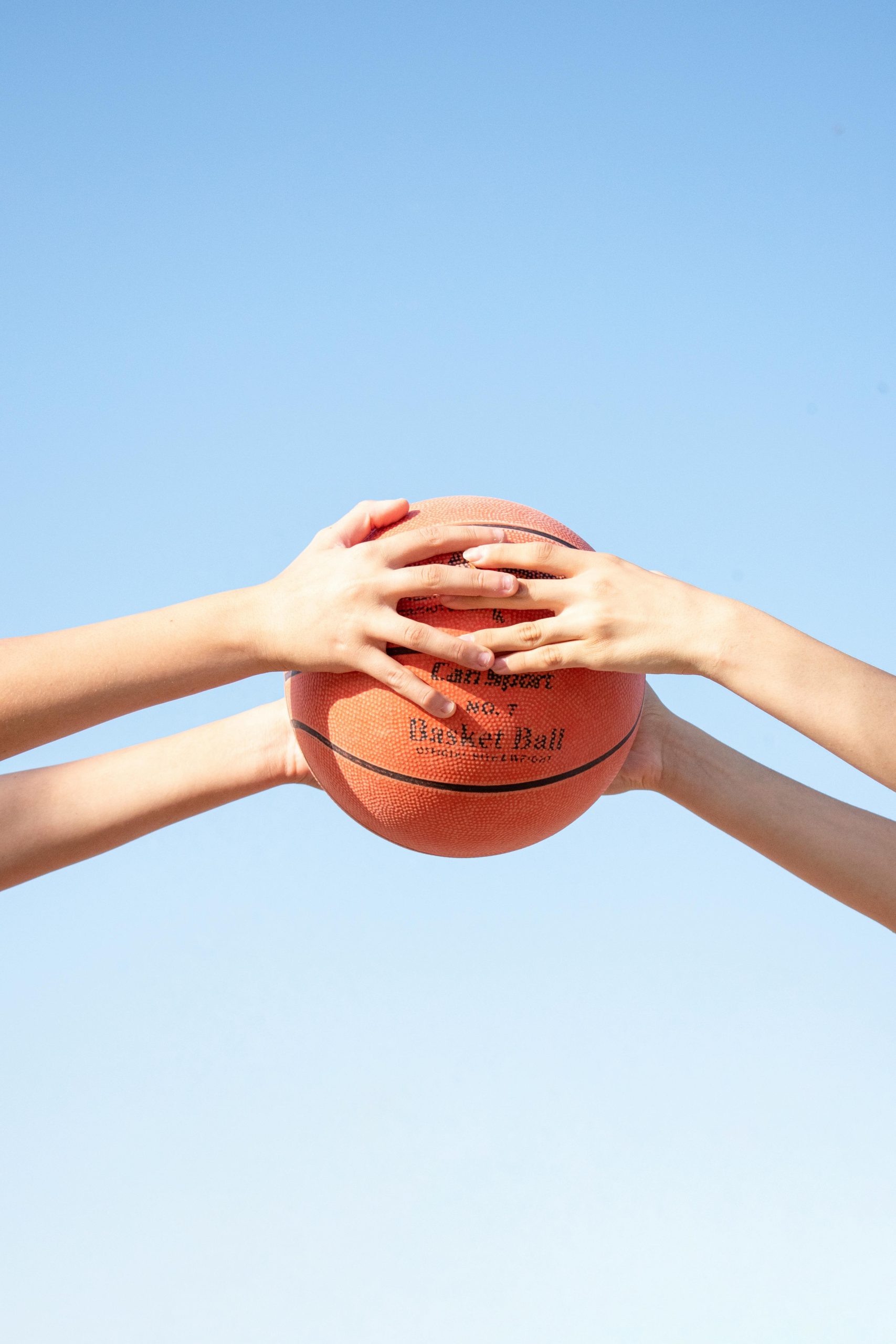 Hands holding basketball under clear blue sky.