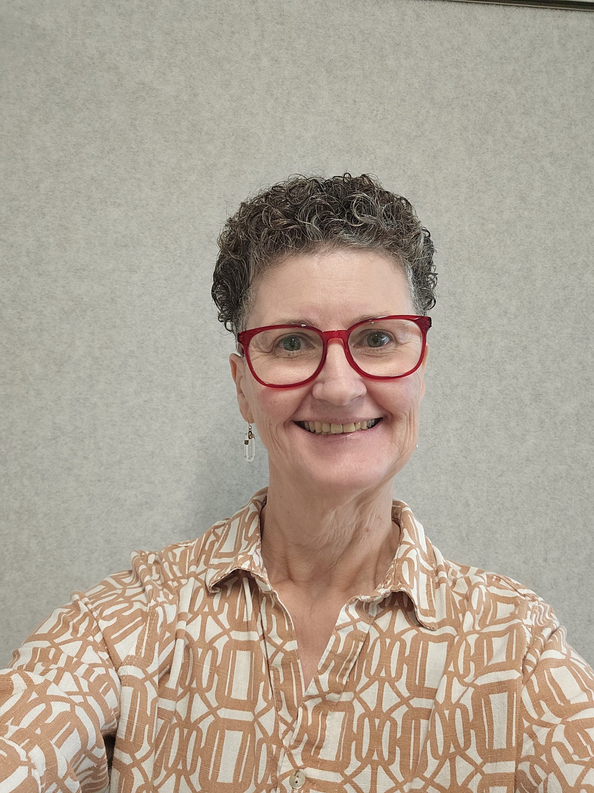 Person smiling, wearing red glasses and patterned shirt.