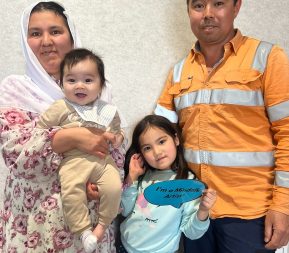 Family with baby and child holding sign smiling.